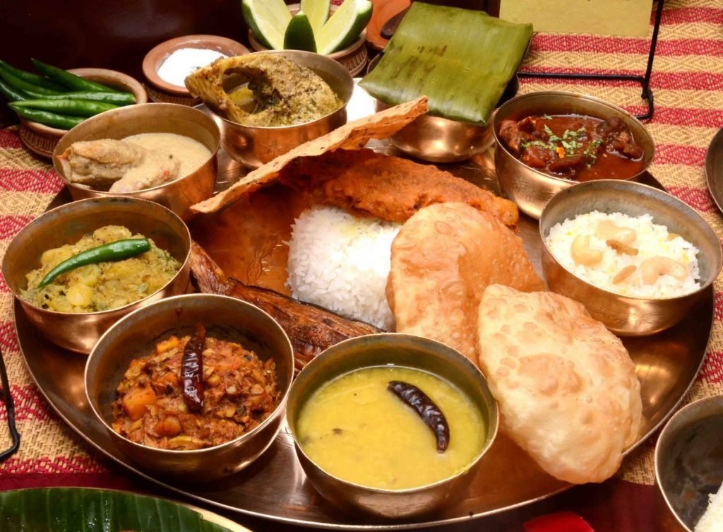 A image of a typical Bengali cuisine. This Bengali thali includes Bhaat, Luchi, Begun Bhaja, Daal, Torkari, Chingri Mach, Sorshe illish, Paturi, Mutton and Payesh.